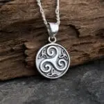 an image of a small Sterling Triskelion-Trinity Pendant. The pendant is round and in the center is the Triskele Celtic Symbol meaning three legged and in the small spaced around the Triskele symbol are three small Triquetra or Trinity Knots. There is oxidation on the background of the circle and the triskele is raised up a bit. The pendant height is .55 inches