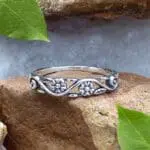 A photo of our Sterling Silver Dainty Double Flower Ring in a narrow filigree band with 3 delicate flowers and leaves amidst a swirl design with the back side being solid.