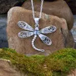 an image of a Sterling Silver Whimsical Dragonfly Pendant. The four wings are solid half of the way and the ends are an open filigree with the tail curving to the right giving it a look of being in flight