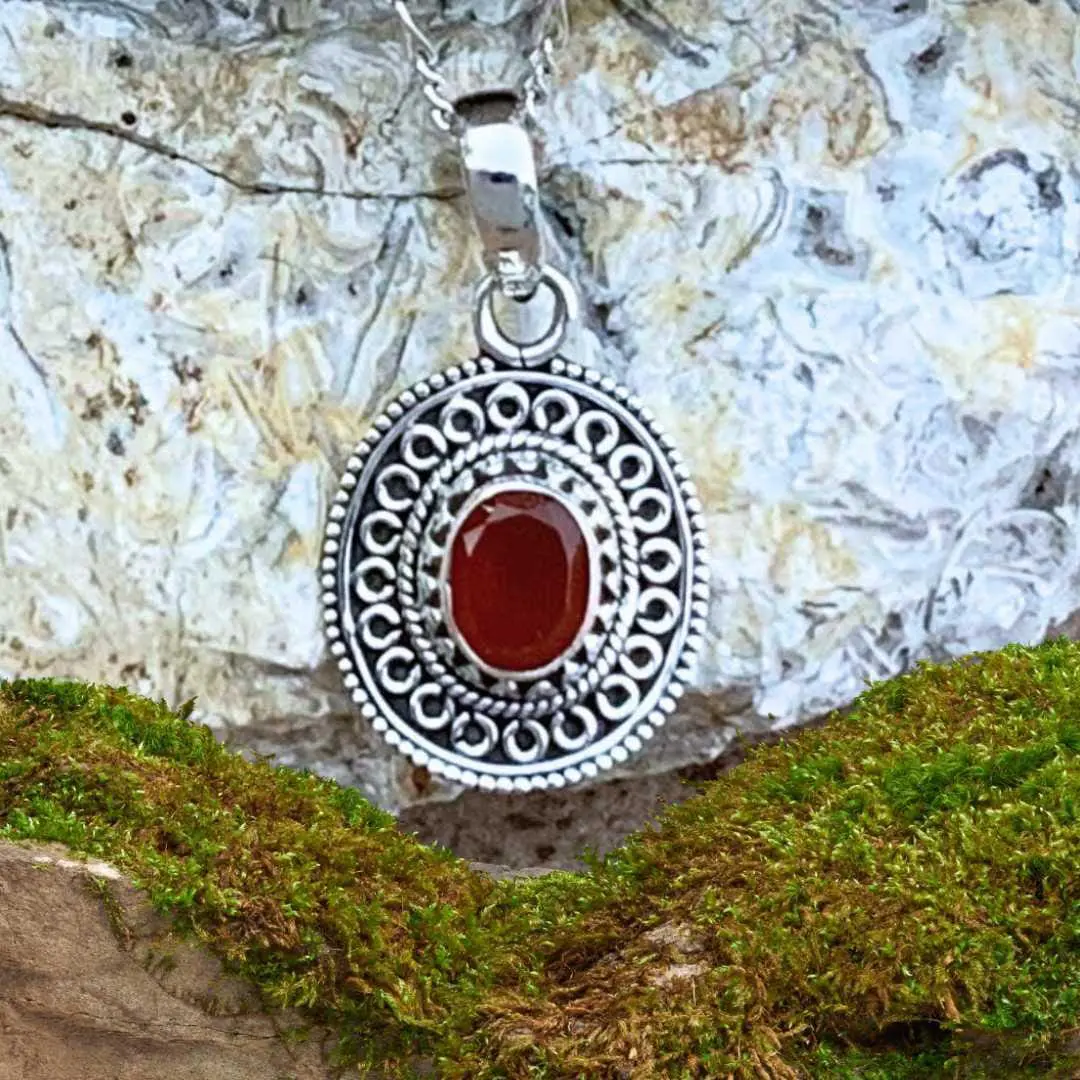 an image of an ornate sterling silver oval pendant with a faceted oval carnelian gemstone in the center