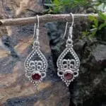 an image of a pair of sterling silver earrings with an upside down open heart and silver beadwork and a small round faceted garnet at the bottom.