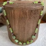 an image of a Faceted Garnet and Peridot Beaded Necklace. The necklace features 7 peridot nuggets in the center with small faceted garnets in between and the pattern going up the neck is alternating small garnets with faceted rondelle peridot. It has a sterling silver lobster clasp