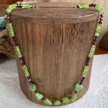 an image of a Faceted Garnet and Peridot Beaded Necklace. The necklace features 7 peridot nuggets in the center with small faceted garnets in between and the pattern going up the neck is alternating small garnets with faceted rondelle peridot. It has a sterling silver lobster clasp