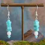 an image of a pair of Square Stacked Amazonite with Pearl Earrings with five 3 x 6 mm square beads stacked on top of a freshwater pearl and framed with a small amethyst rondelle bead on top and bottom. They hang on a sterling silver ear hook.