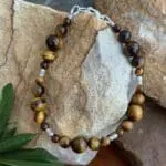 an image of a 7.25 inch long Tiger's Eye bracelet made with 3 sizes of round beads and four dainty silver beads with a primitive flower hand stamped and made by Karen Hill Tribe in Thailand. There is a sterling silver lobster clasp.