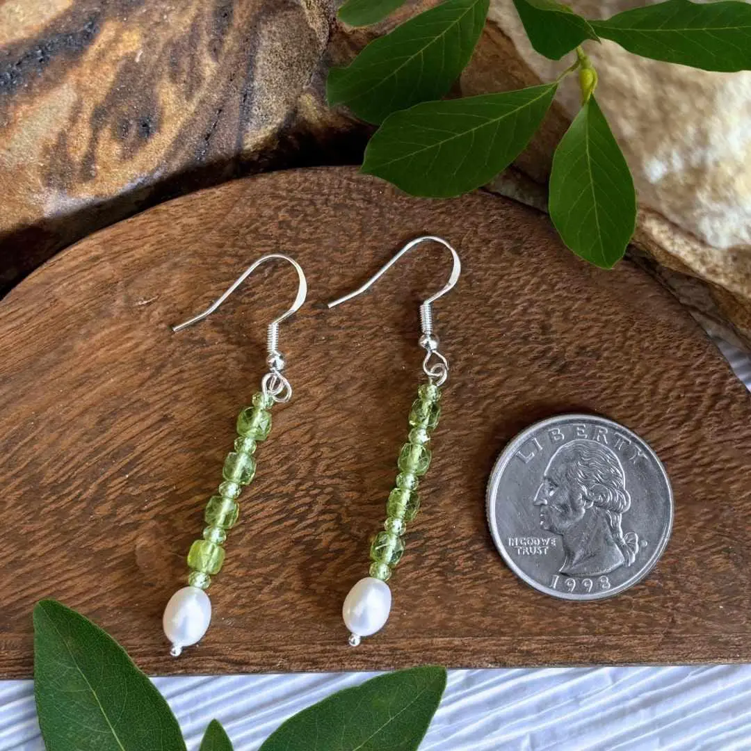 an image of a pair of Stacked Faceted Peridot and Pearl Earrings with 4 faceted peridot cubes spaced with small faceted round peridot beads and anchored by a freshwater pearl. They have a nice amount of dangle and are on a sterling silver earring hook