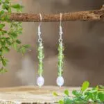 an image of a pair of Stacked Faceted Peridot and Pearl Earrings with 4 faceted peridot cubes spaced with small faceted round peridot beads and anchored by a freshwater pearl. They have a nice amount of dangle and are on a sterling silver earring hook