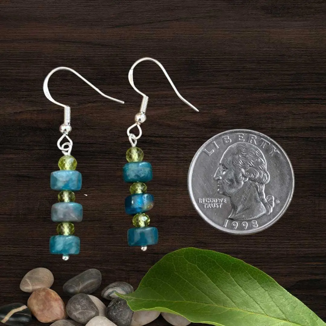 an image of a pair of Apatite Heishi and Faceted Peridot Earrings with three apatite Heishi beads and three 4mm faceted peridot earrings in a stack design on a sterling silver ear hook. The are next to a quarter.