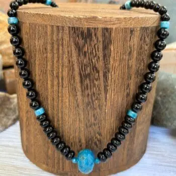 an image of an Apatite and Black Onyx Necklace featuring one large faceted rondelle of blue apatite in the center and rondelle and round black onyx beads working up the neck with occasional apatite heishi beads interspersed.