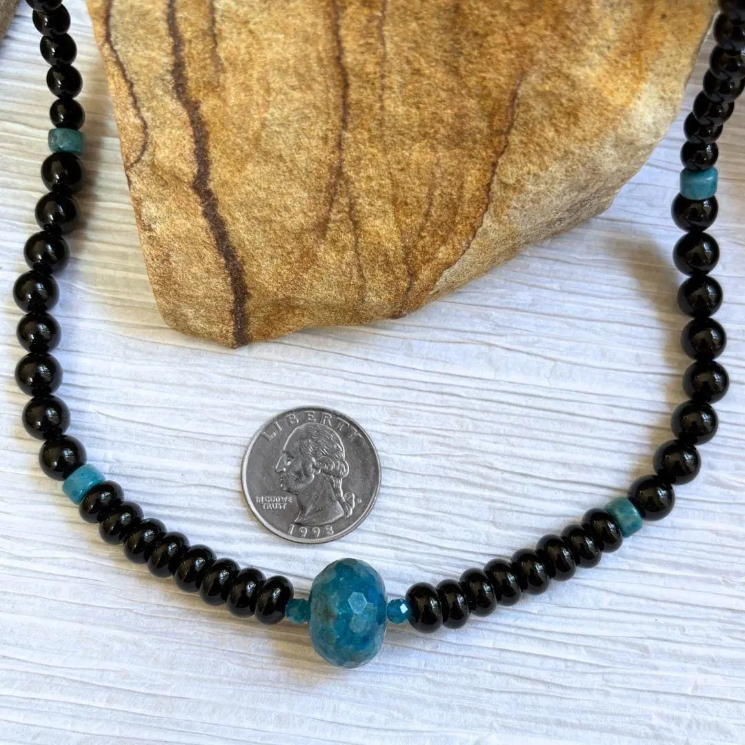an image of an Apatite and Black Onyx Necklace featuring one large faceted rondelle of blue apatite in the center and rondelle and round black onyx beads working up the neck with occasional apatite heishi beads interspersed.
