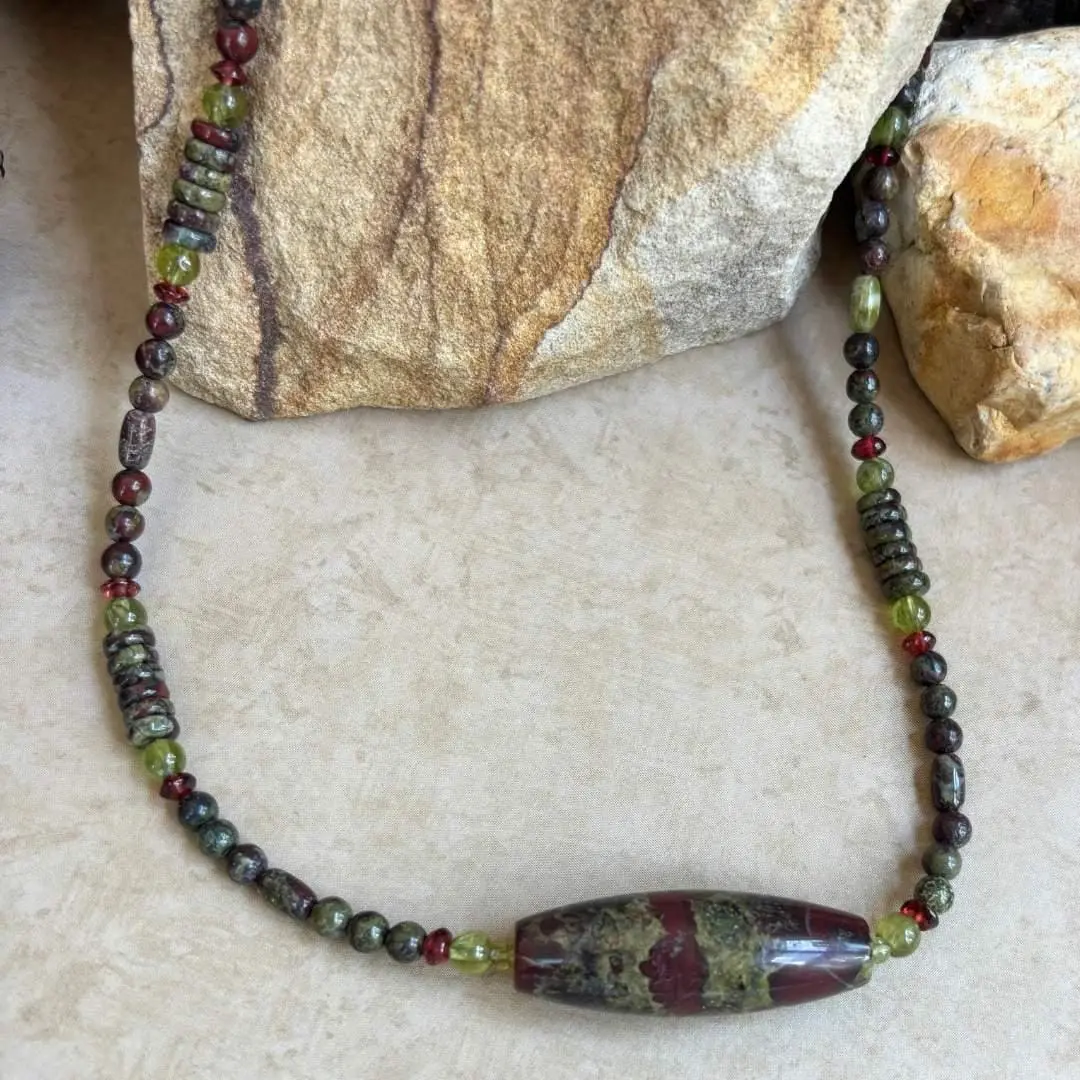 an image of a Dragon Blood Jasper with Peridot and Garnet Gemstone Necklace featuring a large barrel bead of dragon blood jasper with accents of small rondelle garnets and round peridot beads and assorted shapes of dragon blood jasper beads.