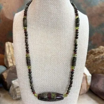 an image of a Dragon Blood Jasper with Peridot and Garnet Gemstone Necklace featuring a large barrel bead of dragon blood jasper with accents of small rondelle garnets and round peridot beads and assorted shapes of dragon blood jasper beads.