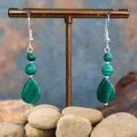 an image of a pair of Teardrop Malachite and Sterling Silver Earrings featuring a teardrop shaped malachite bead at the bottom, then a round smooth malachite bead above it with a smaller one on the ery top. The malachite beads are all separated with a 2mm sterling silver bead and hang on a sterling silver earring hook.