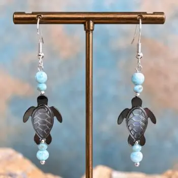 An image of a pair of Larimar and Black Mother of Pearl Sea Turtle Earrings. The earrings have a round smooth larimar bead and a smaller faceted larimar bead with a hand carved Black Mother of Pearl Sea Turtle and another set of the same larimar beads on top. They are on a sterling silver earring hook