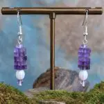 an image of a pair of Square Stacked Amethyst with Pearl Earrings with five 3 x 6 mm square beads stacked on top of a freshwater pearl and framed with a small amethyst rondelle bead on top and bottom. They hang on a sterling silver ear hook.