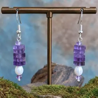 an image of a pair of Square Stacked Amethyst with Pearl Earrings with five 3 x 6 mm square beads stacked on top of a freshwater pearl and framed with a small amethyst rondelle bead on top and bottom. They hang on a sterling silver ear hook.