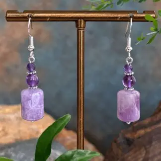 an image of a pair of Amethyst Barrel and Sterling Silver Earrings featuring a barrel shaped rainbow amethyst bead at the bottom, a round approx. 5 mm smooth amethyst bead and topped off with a 4mm faceted amethyst bead. The beads are separated by delicate oxidized sterling silver daisy separator beads and are on a sterling silver earring hook.