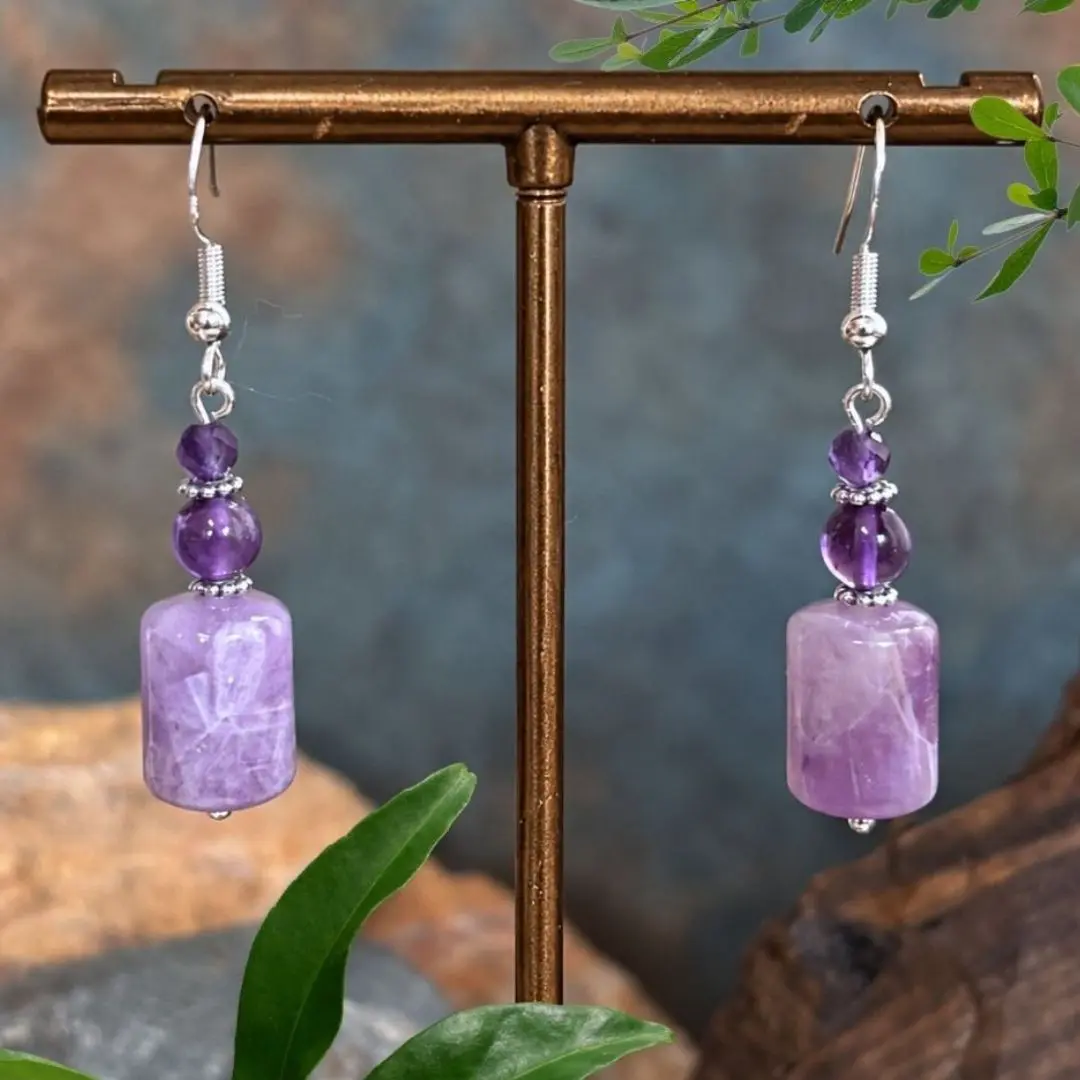 an image of a pair of Amethyst Barrel and Sterling Silver Earrings featuring a barrel shaped rainbow amethyst bead at the bottom, a round approx. 5 mm smooth amethyst bead and topped off with a 4mm faceted amethyst bead. The beads are separated by delicate oxidized sterling silver daisy separator beads and are on a sterling silver earring hook.