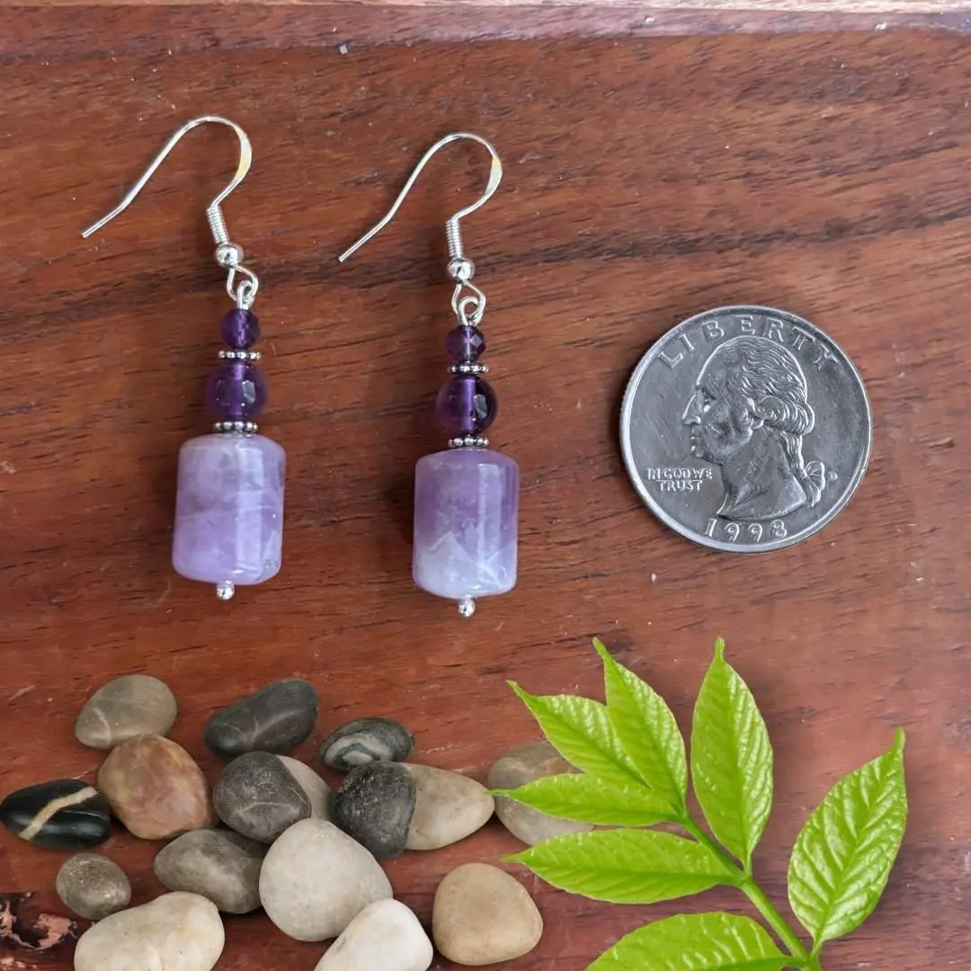 an image of a pair of Amethyst Barrel and Sterling Silver Earrings featuring a barrel shaped rainbow amethyst bead at the bottom, a round approx. 5 mm smooth amethyst bead and topped off with a 4mm faceted amethyst bead. The beads are separated by delicate oxidized sterling silver daisy separator beads and are on a sterling silver earring hook.