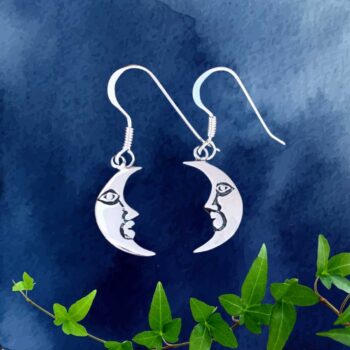 an image of a pair of sterling silver earrings that have a modest dangle. Each angle is a waning crescent moon shape with a face on it.