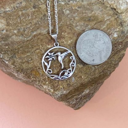 an image of an open sterling silver circle pendant with a hummingbird in flight drinking nectar from a blooming flower