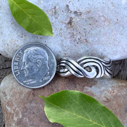 an image of a sterling silver ring with a design that looks like braided waves. The ring is next to a dime for perspective