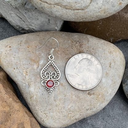 An image of a sterling silver earring with an open upside down heart and a round faceted garnet next to a quarter