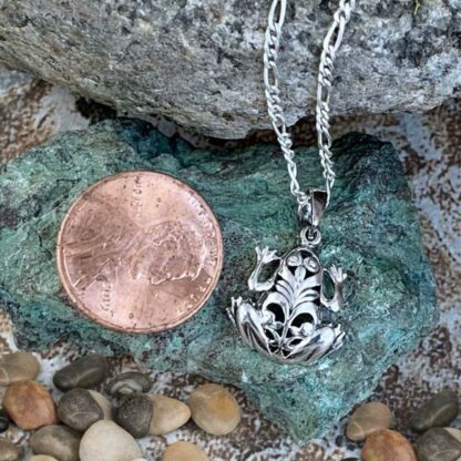 A sterling silver filigree frog pendant next to a penny for perspective.