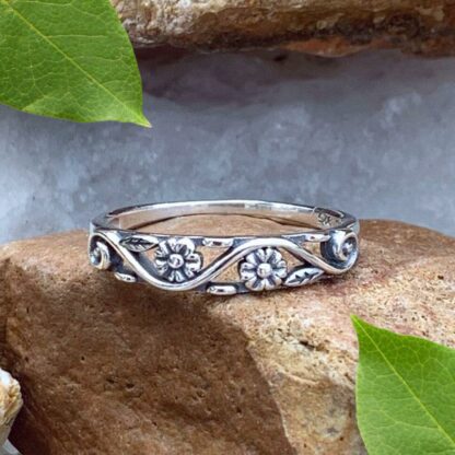 A photo of our Sterling Silver Dainty Double Flower Ring in a narrow filigree band with 3 delicate flowers and leaves amidst a swirl design with the back side being solid.