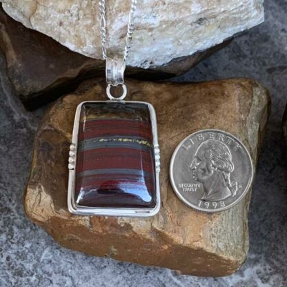 Rectangular Tiger Iron Stone and Sterling Silver Pendant Next to Quarter