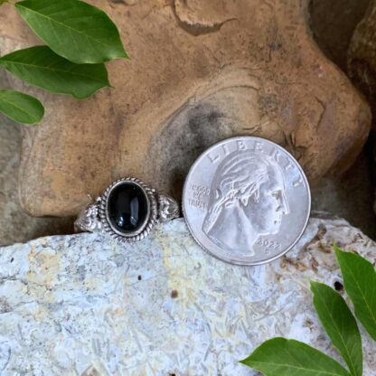 An image of an Oval Black Onyx and Sterling Silver Ring with a silver heart on each side. The ring is next to a quarter