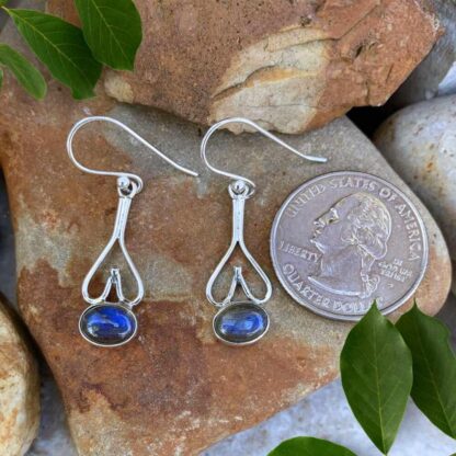 Upside down open sterling silver hearts with a horizontally placed oval labradorite gemstone at the bottom of these dangle sterling silver and labradorite earrings. In this image the earrings are next to a quarter for perspective.