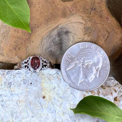 An image of our Petite Faceted Oval Garnet and Filigree Sterling Silver Ring Next to Quarter