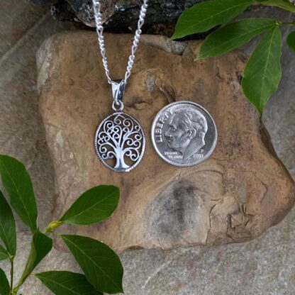 An image of a Petite Oval Sterling Silver Swirling Tree of Life Pendant with a total drop of .748 inches. The pendant is next to a dime