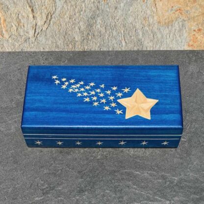 An image of a rectangle shaped handcrafted cobalt shade blue keepsake box with one large star and many small stars in a shooting star pattern on top. It has a band of white stars around the bottom edge. Inside is a layer of red velvet to lay your items on. Dimensions are 7.125 in. x 3.5 in. x 1.75 in.