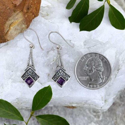 an image of an elegant pair of sterling silver dangle earrings that have two pieces of sterling silver dropping down to a square diamond shape with oxidation and a bit of a small swirl accent design and then a faceted square amethyst at the base angled in a diamond shape.