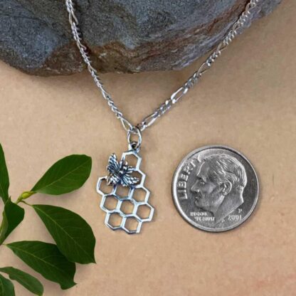 an image of a sterling silver open honeycomb with a bee on the top left corner. The pendant is next to a dime