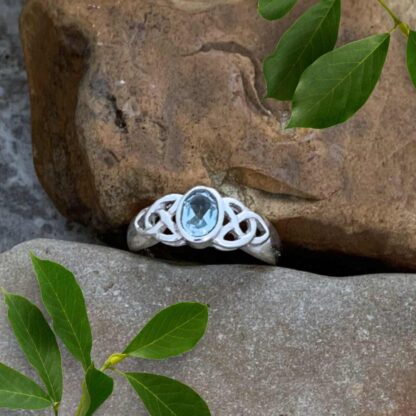 an image of our Sterling Silver and Oval Blue Topaz Celtic Ring. An oval faceted gemstone in the center with a Celtic knot on each side of the stone 