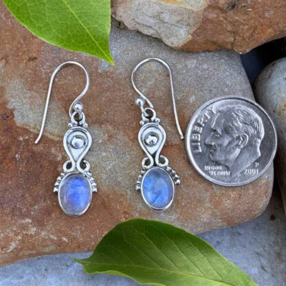 an image of a pair of Sterling Silver and Oval Rainbow Moonstone Earrings next to a dime. These are dainty with a slight amount of dangle