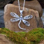 an image of a Sterling Silver Whimsical Dragonfly Pendant. The four wings are solid half of the way and the ends are an open filigree with the tail curving to the right giving it a look of being in flight
