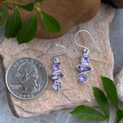 an image of a pair of Triple Amethyst and Sterling Silver Dangle Earrings with the top amethyst being square, the middle in a marquise shape and the bottom one is round.