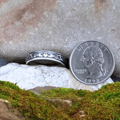 An image of our Narrow Sterling Silver Claddagh Band Ring Next to a quarter