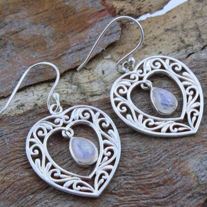 a image of a pair of Sterling Silver and Rainbow Moonstone Heart Earrings. An open filigree sterling silver heart with a teardrop shaped rainbow moonstone that dangles in the center of the heart.