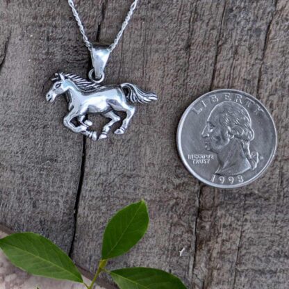 an image of a sterling silver galloping horse pendant next to a quarter