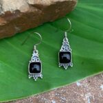 an image of a pair of Dainty Black Onyx and Sterling Silver Dangle Earrings with a square black onyx and sterling silver beadwork underneath the stone and a delicate pattern of sterling silver on top of the stone