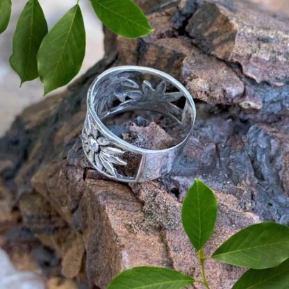 an image of a rear view of a wide sterling silver ring with daisies wrapping around as the design tapers toward the back.