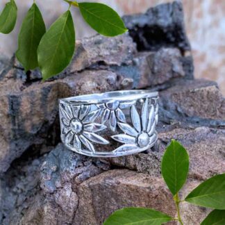 an image of a wide sterling silver ring with daisies wrapping around as the design tapers toward the back.