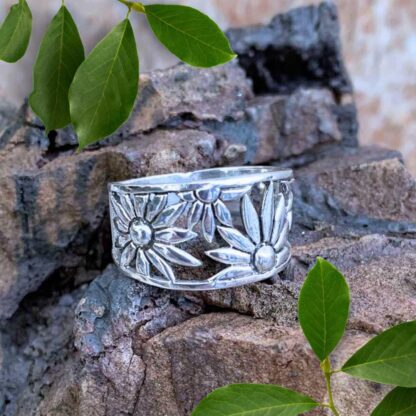 an image of a wide sterling silver ring with daisies wrapping around as the design tapers toward the back.