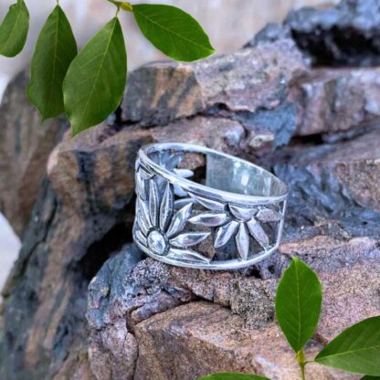 an image of a side view of a wide sterling silver ring with daisies wrapping around as the design tapers toward the back.