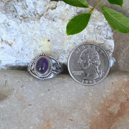 an image of an Oval Amethyst Cabochon and Sterling Silver Ring with a spiral design on each side. The ring is next to a quarter